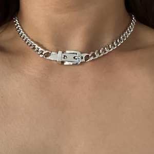 High-shine silver belt buckle focal point on a flat Cuban link chain, worn as a snug choker for a modern grunge look.