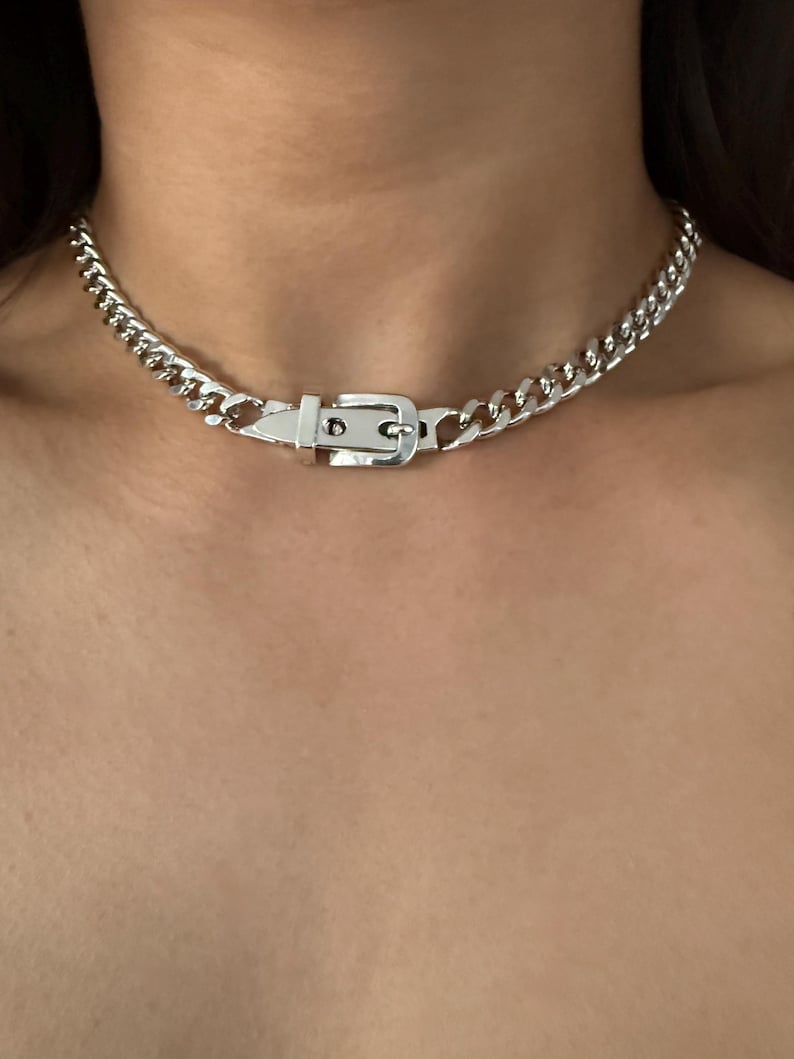High-shine silver belt buckle focal point on a flat Cuban link chain, worn as a snug choker for a modern grunge look.