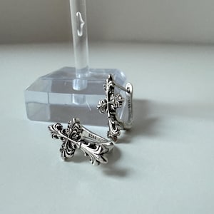 Könnte beinhalten: Ein Paar silberfarbene Creolen mit Kreuzdesign. Die Ohrringe haben ein aufwendiges, detailliertes Muster und werden auf einer weißen Oberfläche präsentiert. Die Ohrringe sind mit "S925" gekennzeichnet.