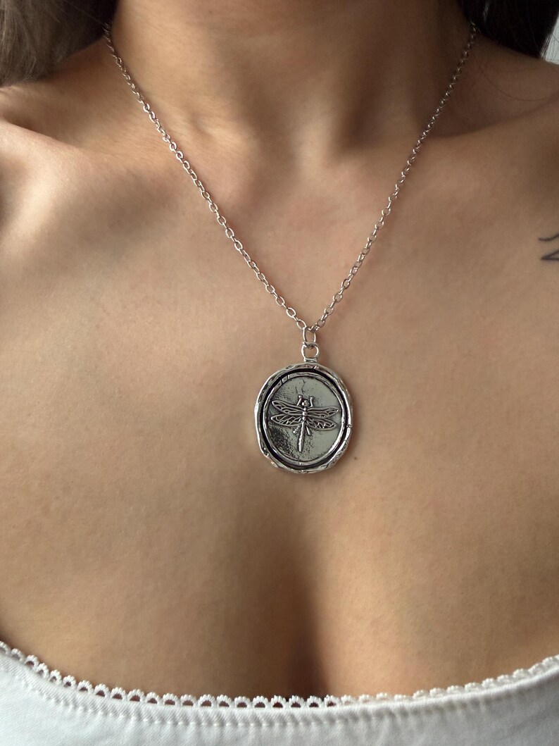 Symbolic Transformation Charm Detail: A sharp product view focusing on the embossed dragonfly within the oval seal, illustrating its "Modern Amulet" aesthetic.