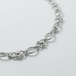 Macro photography of a silver-tone gothic necklace focusing on the unique "pierced" link structure and the polished, tarnish-resistant surface of the steel.