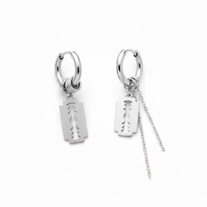 Könnte beinhalten: Ein Paar silberfarbene Creolen. Jeder Ohrring hat einen kleinen, rechteckigen Anhänger in Form einer Rasierklinge. Ein Ohrring hat eine Kette. Der Hintergrund ist weiß.