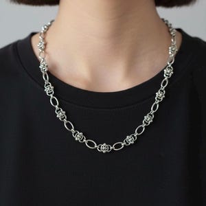 A 12mm wide stainless steel gothic chainmail necklace displayed in a full oval on a clean white studio background, showcasing the intricate industrial pierced link design.