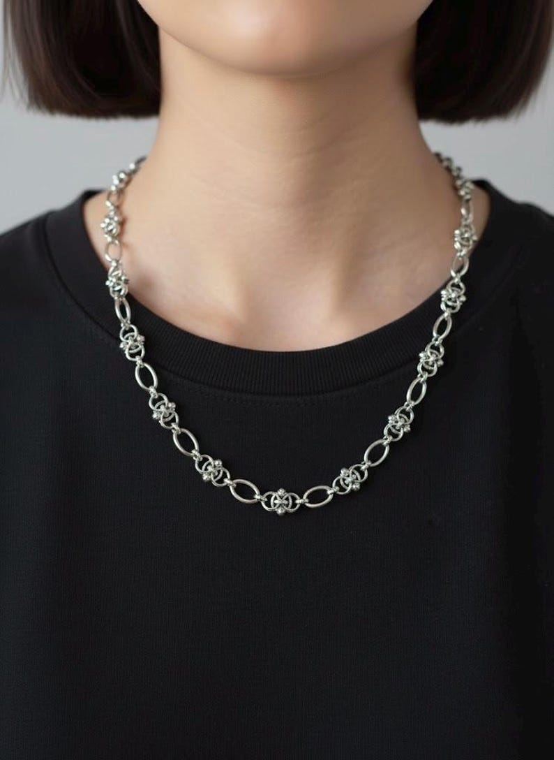 A 12mm wide stainless steel gothic chainmail necklace displayed in a full oval on a clean white studio background, showcasing the intricate industrial pierced link design.