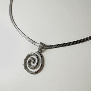 A clear, professional product shot of the stainless steel snake chain and hypnotic swirl pendant, emphasizing its tarnish-proof and waterproof properties.