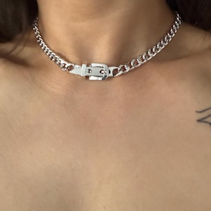 Front-facing view of a silver buckle choker on a model, showcasing its bold industrial aesthetic and how it sits at the hollow of the throat.