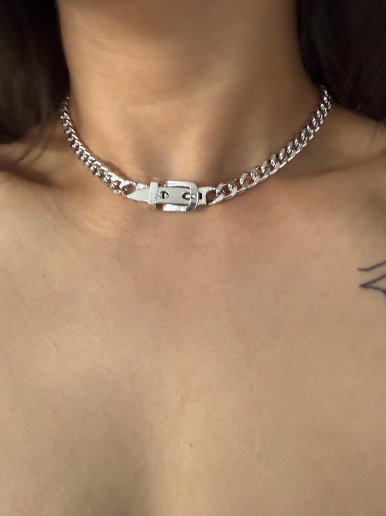 Front-facing view of a silver buckle choker on a model, showcasing its bold industrial aesthetic and how it sits at the hollow of the throat.