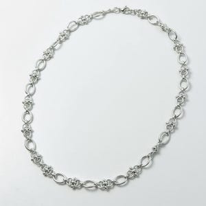 Side profile view of a heavy 60cm stainless steel industrial chain at a 45-degree angle, highlighting the depth and texture of the metallic chainmail links.