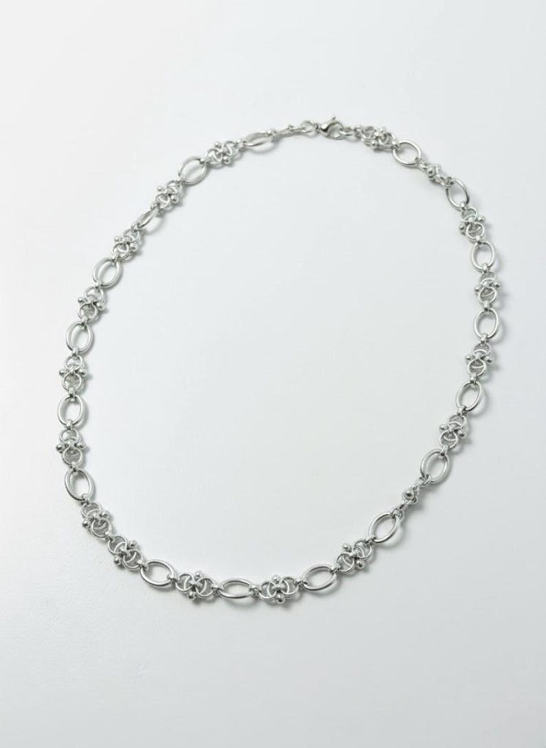 Side profile view of a heavy 60cm stainless steel industrial chain at a 45-degree angle, highlighting the depth and texture of the metallic chainmail links.