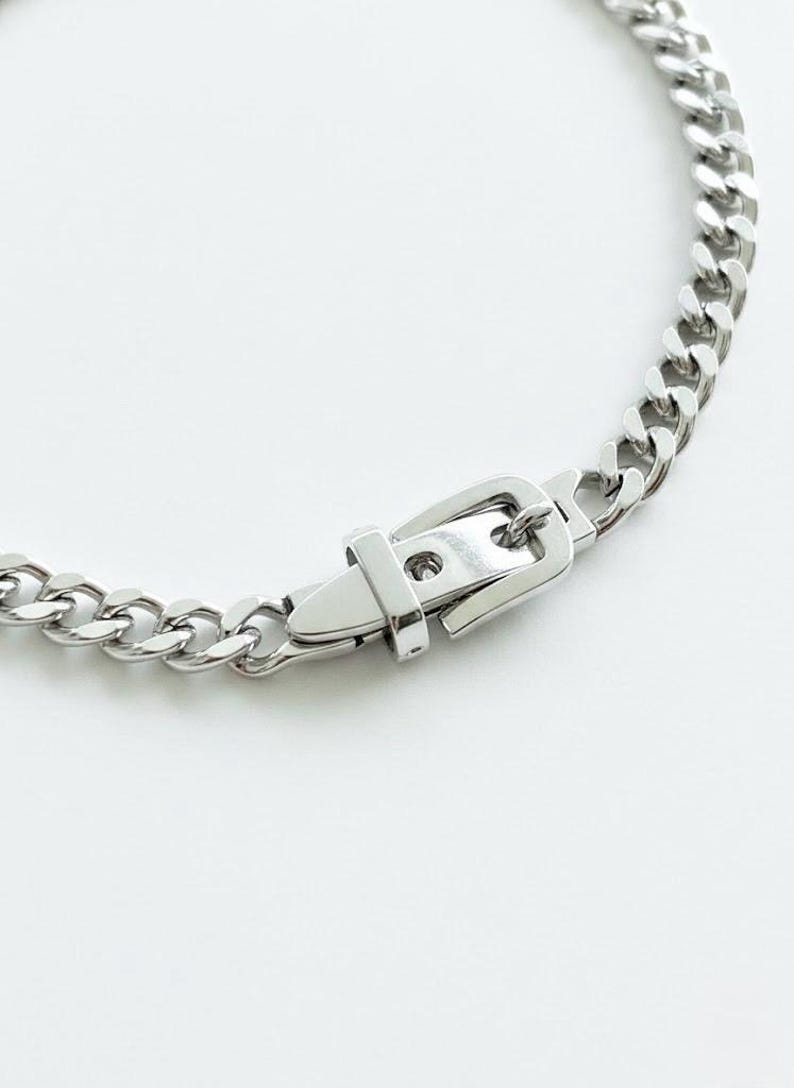 Flat lay of the silver Cuban link chain and buckle closure on a white surface, highlighting the heavyweight industrial design.