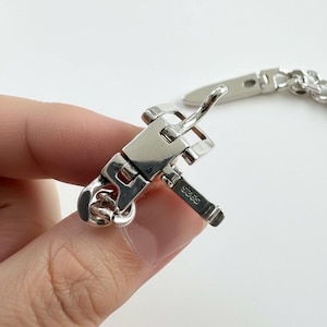 A hand holding the open buckle mechanism, revealing the intricate hinge work and high-polish silver luster.