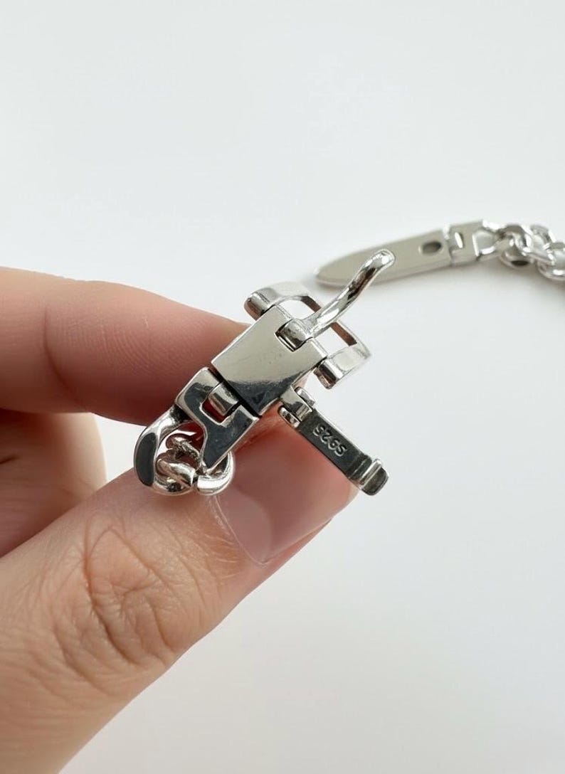 A hand holding the open buckle mechanism, revealing the intricate hinge work and high-polish silver luster.