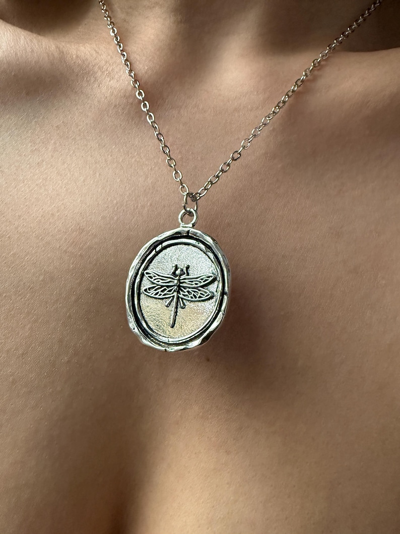 Dark Cottagecore Jewelry Flatlay: An overhead view of the dragonfly medallion, showcasing the antique-inspired hardware and the vertical oval drop silhouette.