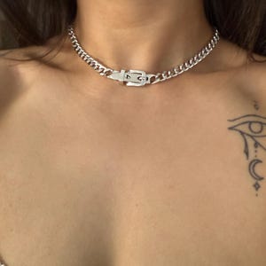Detailed shot of a silver Cuban link choker with a belt buckle closure, highlighting the polished finish and edgy streetwear style.