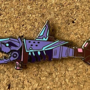 May include: A purple and blue enamel pin of a robot shark with a detailed design. The robot shark has a large fin on its back and a gun on its side.