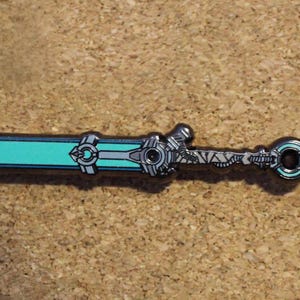 May include: A detailed pin featuring a stylized sword design. The pin has a teal blade with silver accents and a detailed hilt. The pin is set against a neutral background.