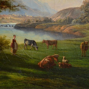 Op de afbeelding: Een schilderij dat een pastorale sc&egrave;ne voorstelt met een vrouw die in een veld staat met koeien en schapen. De sc&egrave;ne speelt zich af in een vallei met een rivier en bergen op de achtergrond. Het schilderij is gemaakt in een realistische stijl met gedempte kleuren.