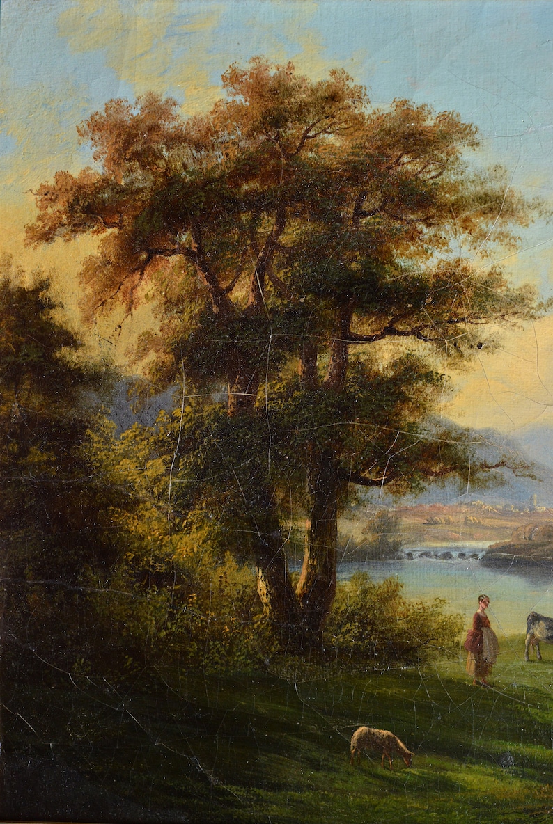 Op de afbeelding: Een schilderij van een landelijk landschap met een grote boom op de voorgrond, een vrouw en een koe in de verte en een brug over een rivier.