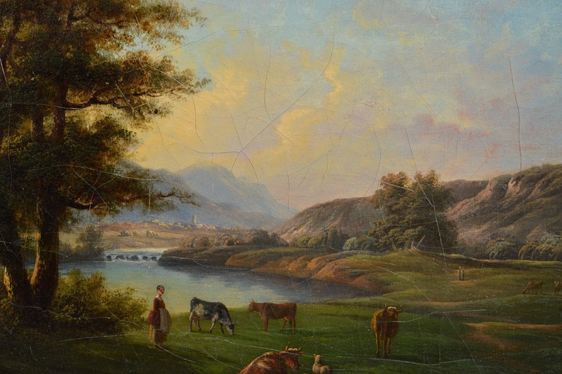 Op de afbeelding: Een schilderij dat een landelijk landschap afbeeldt met een rivier, glooiende heuvels en een klein dorp in de verte. De sc&egrave;ne is in warm, gouden licht gebaad, met een paar koeien die grazen in een weide bij de rivier. Een vrouw in een lange jurk staat aan de oever van de rivier en kijkt naar de koeien.