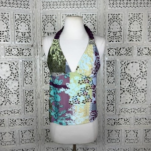 May include: A sleeveless halter top featuring a patchwork design with various floral and geometric patterns in shades of green, light blue, yellow, and deep purple. The garment has a deep V-neckline and a braided dark purple strap around the neck.