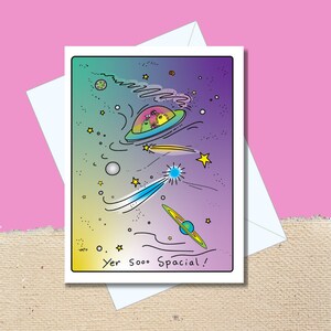 Peut inclure: Une carte de vœux avec une illustration colorée de dessin animé d'un vaisseau spatial volant dans l'espace avec des étoiles et des planètes. Le texte sur la carte dit "Yer sooo spacial!"