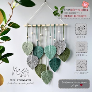 May include: A macrame wall hanging with a wooden dowel and green, gray, and white leaves. The wall hanging is made of cotton cord and is a unique and eco-friendly gift idea. "Free gift wrapping and cards with custom messages." "Macrame art by Meii"