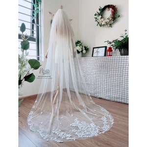May include: A white bridal veil with a delicate floral design. The veil is made of soft tulle and features a scalloped edge. The veil is displayed on a mannequin.