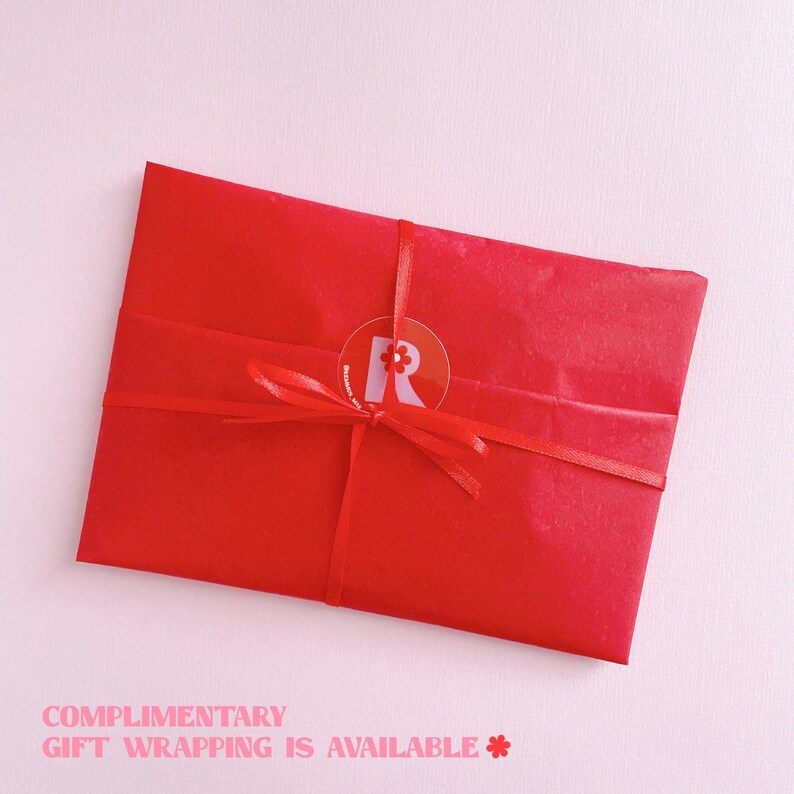 Puede incluir: Una bolsa de regalo roja con una cinta roja atada alrededor. La bolsa tiene una pegatina blanca con una letra roja "R" y una peque&ntilde;a flor en ella. El texto "COMPLIMENTARY GIFT WRAPPING IS AVAILABLE*" est&aacute; impreso debajo de la imagen.