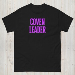 Op de afbeelding: Zwart T-shirt met de tekst "COVEN LEADER" in paars.