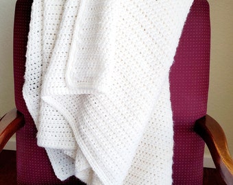 May include: A white crocheted blanket draped over a burgundy armchair. The blanket is folded and has a textured, woven pattern.