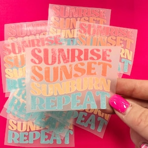 May include: A stack of clear vinyl sheets with the text "Sunrise Sunset Sunburn Repeat" printed in rainbow colors. The text is in a retro font style.
