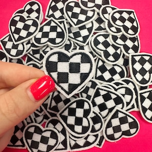 May include: A pile of black and white checkered heart-shaped patches. The patches are made of felt and have a white outline.