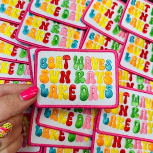 May include: A stack of colorful embroidered iron-on patches with the text "Boat Waves Sun Rays Lake Days". The patches are white with pink borders and feature rainbow-colored letters.