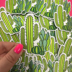 May include: A collection of green and white embroidered cactus patches. The patches feature different styles of cacti, including tall, slender cacti with spines and smaller, round cacti with flowers.