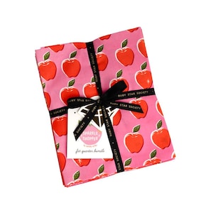 Peut inclure: Un lot de tissus pliés présentant un motif répétitif de pommes rouges avec des feuilles vertes sur un fond rose. L'ensemble est noué avec un ruban noir portant le texte Ruby Star Society et comprend une étiquette blanche marquée Sparkle Shopper.