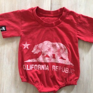 May include: Red baby onesie with a white graphic of a bear and a star, with the text "CALIFORNIA REPUBLIC" underneath.