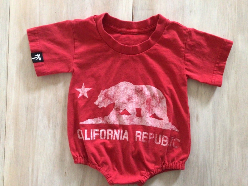May include: Red baby onesie with a white graphic of a bear and a star, with the text "CALIFORNIA REPUBLIC" underneath.