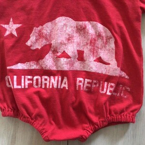 May include: Red baby onesie with a white graphic of the California Republic bear and star. The text "CALIFORNIA REPUBLIC" is printed below the bear.