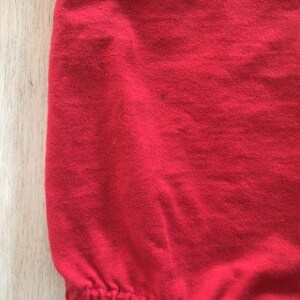 May include: Close-up of a red fabric with a smooth texture. The fabric is slightly wrinkled and has a soft, comfortable feel.