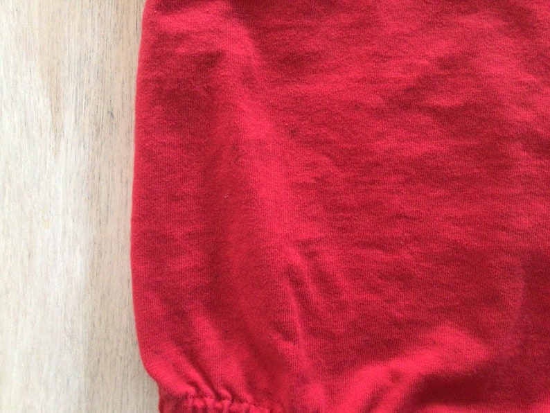May include: Close-up of a red fabric with a smooth texture. The fabric is slightly wrinkled and has a soft, comfortable feel.