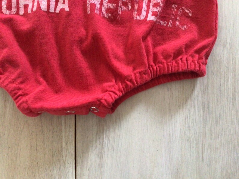 May include: Red baby onesie with white text that reads "California Republic".