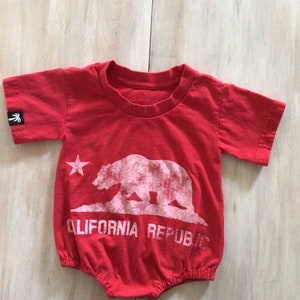 May include: Red baby onesie with a white graphic of the California bear and the text "CALIFORNIA REPUBLIC".