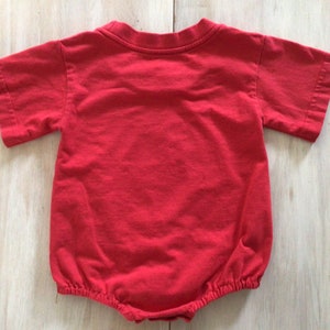 May include: Red short-sleeved baby onesie with a gathered bottom.