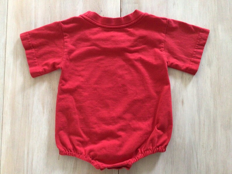 May include: Red short-sleeved baby onesie with a gathered bottom.