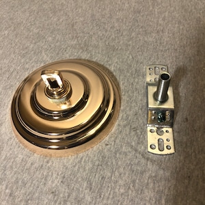 May include: A gold-toned metal ceiling fixture with a round canopy and a hook. The fixture is designed for hanging a light fixture. The fixture also includes a metal mounting plate with holes for attaching to a ceiling.