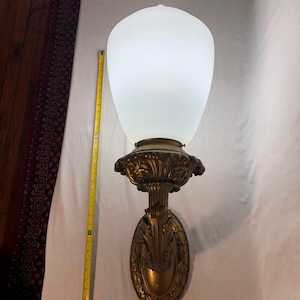 May include: A gold-toned wall sconce with an ornate design and a white frosted glass shade. The sconce is about 18 inches tall.