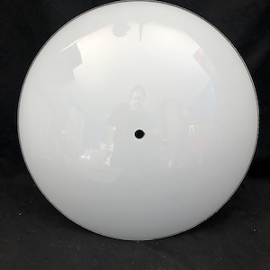 Puede incluir: Una pantalla de lámpara redonda de vidrio blanco con un agujero central negro.