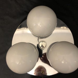 May include: A chrome-finished ceiling light fixture with three white globe-shaped bulbs arranged around a central point. The fixture has a circular base and a hanging wire.