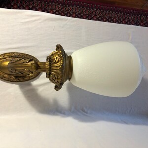 May include: A gold-toned wall sconce with an ornate design and a white frosted glass shade.