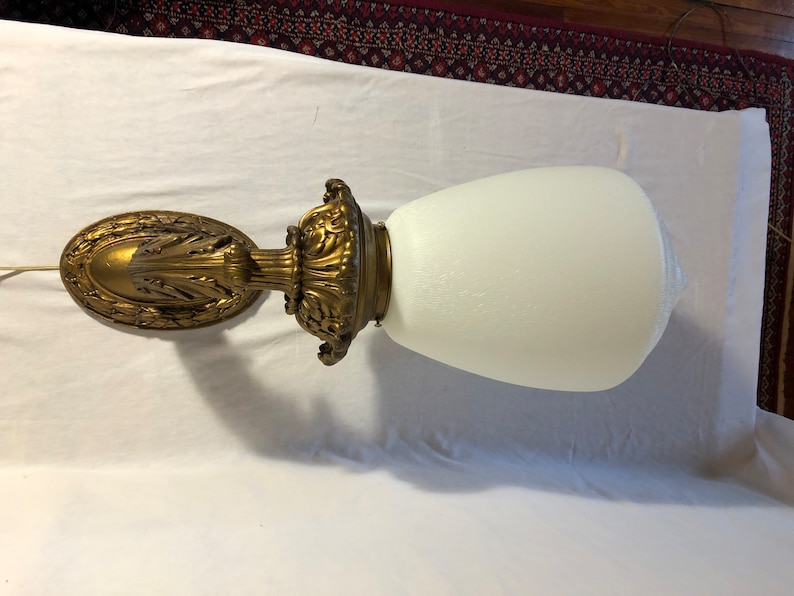 May include: A gold-toned wall sconce with an ornate design and a white frosted glass shade.